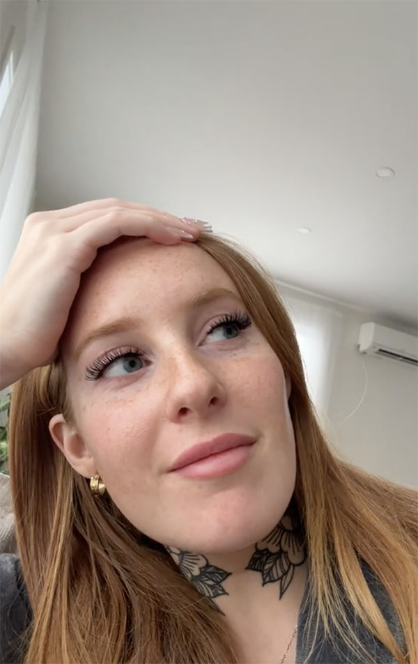 @jademoriisset Femme aux cheveux roux, taches de rousseur et tatouage floral au cou, la main pos&eacute;e sur le front, regardant vers le haut