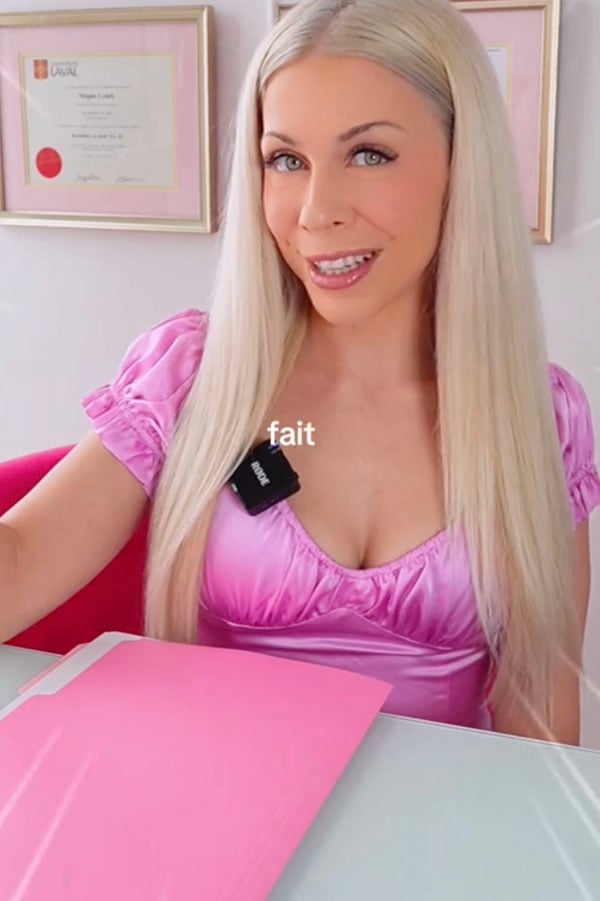 Avocate Rose blonde en robe rose assise &agrave; un bureau avec un dipl&ocirc;me au mur, avec le mot &laquo; fait &raquo; superpos&eacute;